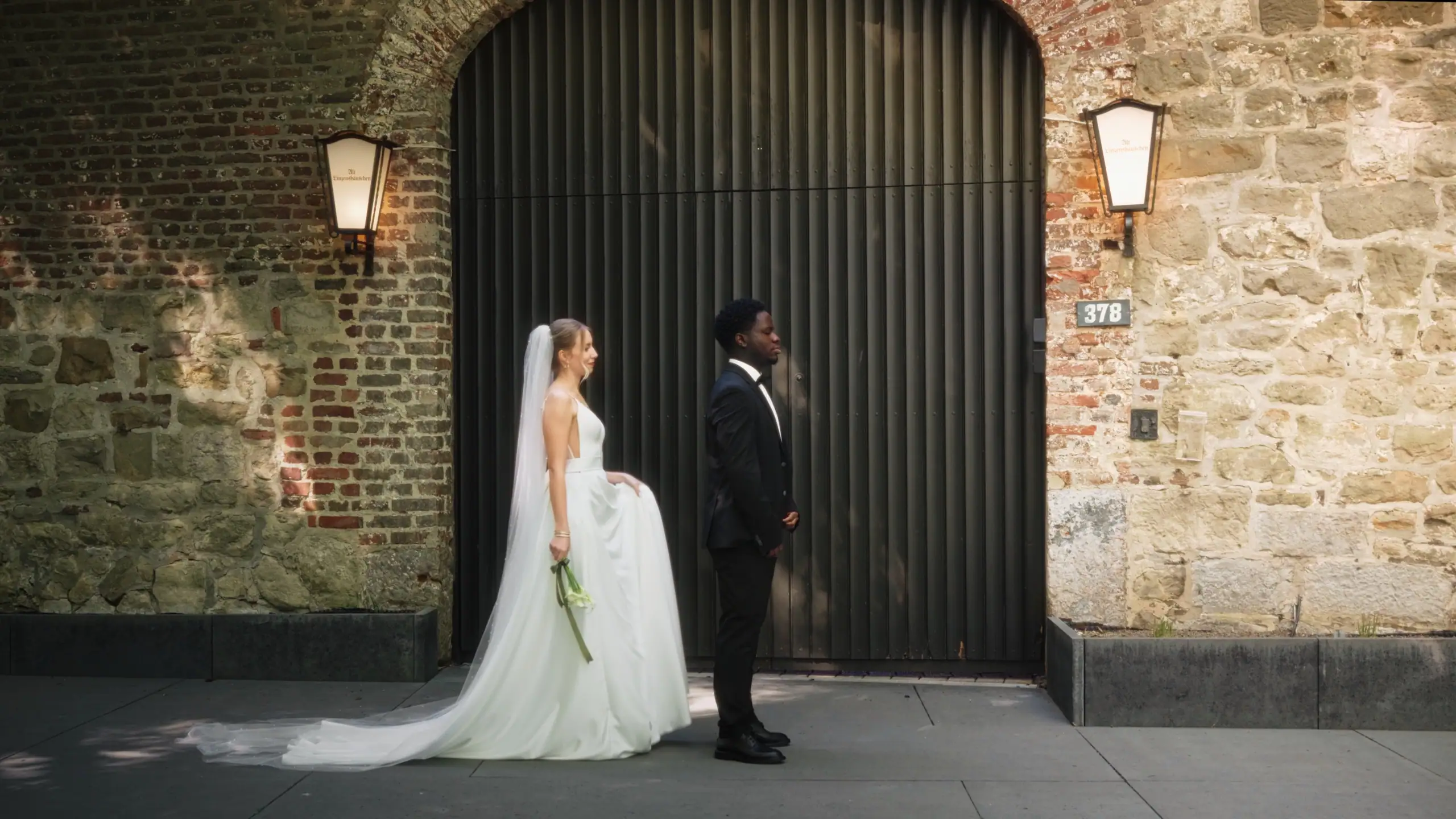 Hochzeitspaar im Sonnenlicht vor einem Fenster mit grünen Bäumen im Hintergrund.